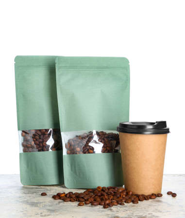 Bags with coffee beans and cup on table against white background