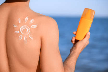 Handsome young man applying sunscreen cream on sea beachの写真素材
