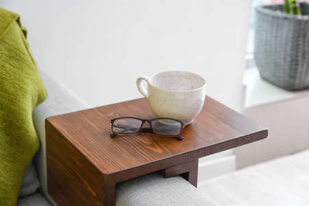 Cup with eyeglasses on armrest table in room