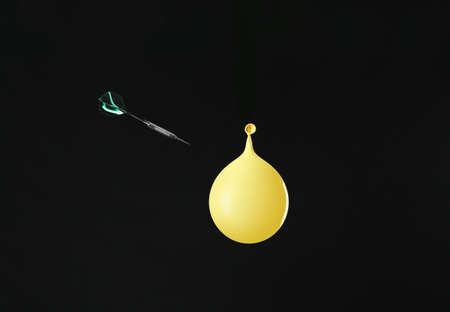 Throwing of dart in balloon with water on dark background