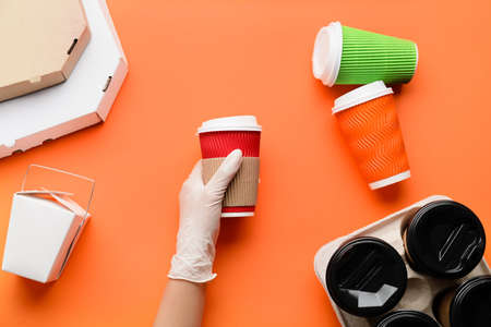 Hand in protective glove and with cups of coffee on color backgroundの写真素材