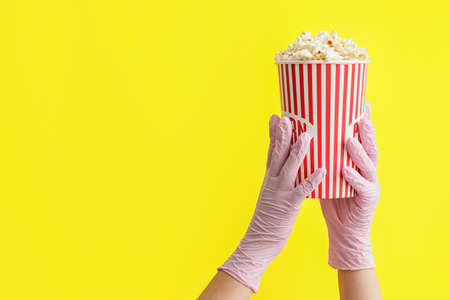 Hands in protective gloves and with popcorn on color backgroundの写真素材