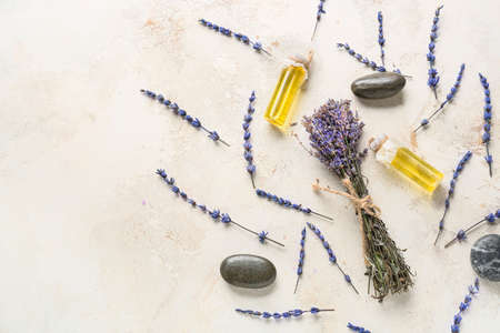 Lavender bouquet and bottles with essential oil on light background