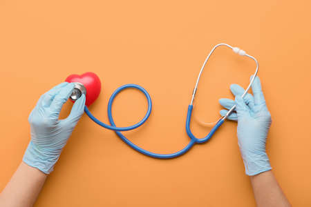 Hands of doctor with stethoscope and heart on color backgroundの写真素材
