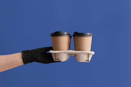 Hand in protective glove and with cups of coffee on color backgroundの写真素材