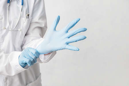 Doctor putting on medical gloves against light backgroundの写真素材