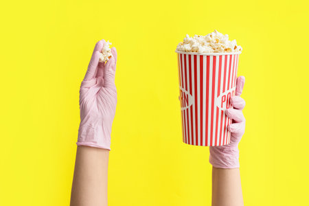 Hands in protective gloves and with popcorn on color backgroundの写真素材