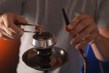 Man putting coal cubes on tobacco bowl closeup