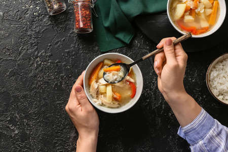 Woman eating tasty rice soup at tableの写真素材