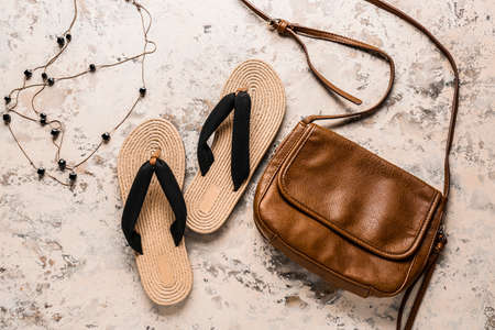 Stylish female bag and flip-flops on color background