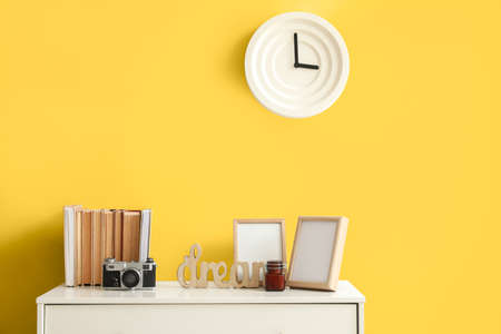 Chest of drawers with books and decor near yellow wall in interior of room