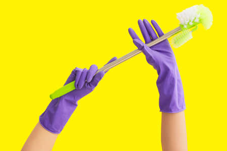 Hands in rubber gloves holding toilet brush on color background