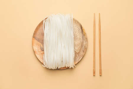 Raw rice noodles with chopsticks on color background