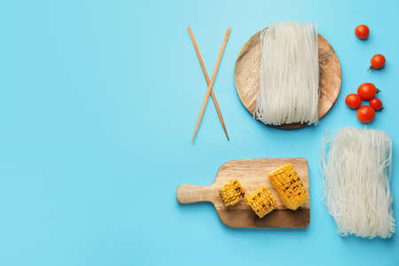 Raw rice noodles with ingredients on color background