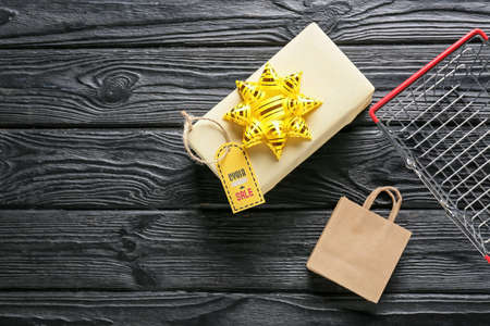 Gift box with shopping bag, basket and tag with text CYBER MONDAY SALE on dark wooden backgroundの写真素材