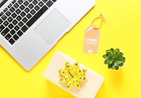 Laptop with gift box and shopping tag with text CYBER MONDAY on color background