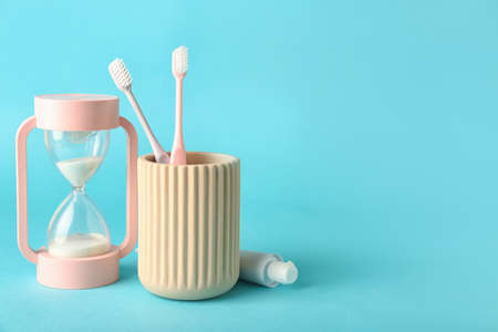 Hourglass, paste and toothbrushes on color background