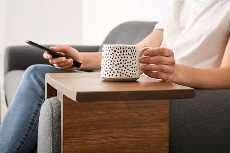Woman with cup of tea watching TV on sofa at homeの写真素材