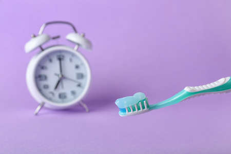 Toothbrush with paste and alarm clock on color background