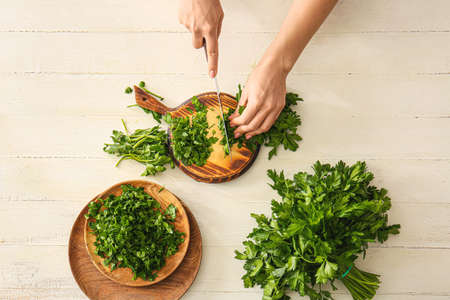 Woman cutting fresh parsley at tableの写真素材