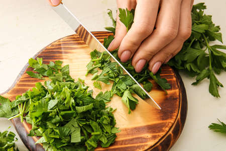 Woman cutting fresh parsley at table, closeup