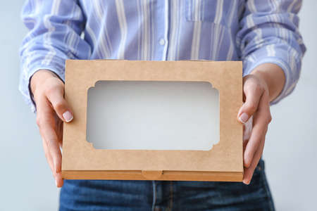 Woman with cardboard box on light background