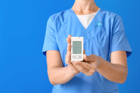 Doctor with digital glucometer on color background. Diabetes conceptの写真素材