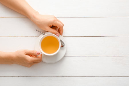 Female hands with cup of green tea on wooden tableの写真素材