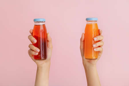 Female hands with bottles of juices on color backgroundの写真素材