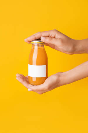 Female hands with bottle of juice on color background
