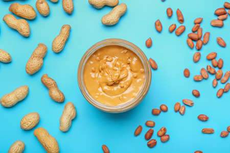 Jar with tasty peanut butter and nuts on color backgroundの写真素材