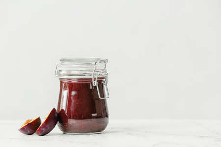 Glass jar with delicious homemade plum jam on white backgroundの写真素材