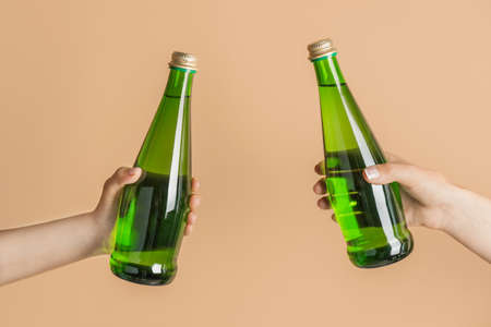 Hands with bottles of clean water on color background
