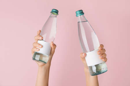 Hands with bottles of clean water on color backgroundの写真素材