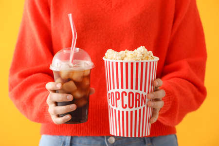 Woman with tasty popcorn and cola on color backgroundの写真素材
