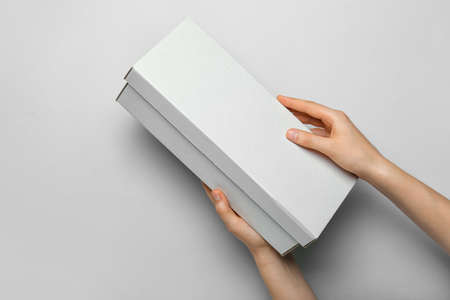 Hands with blank cardboard box on light background