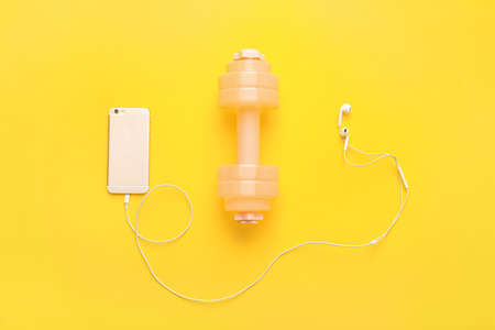 Stylish dumbbell, earphones and mobile phone on color backgroundの写真素材