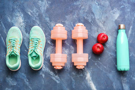 Stylish dumbbells, bottle of water and sports shoes on color backgroundの写真素材