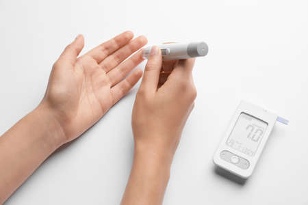 Female hands with lancet pen and glucometer on white background. Diabetes concept