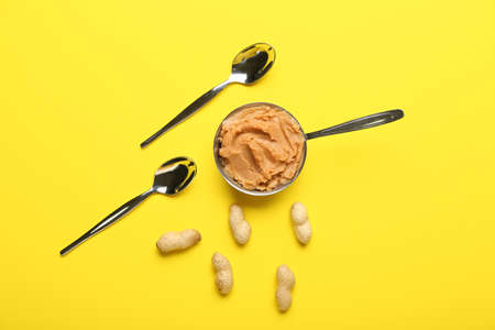 Pot with tasty peanut butter, nuts and spoon on color backgroundの写真素材