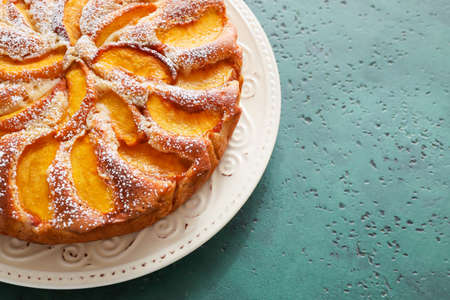 Plate with tasty peach pie on color background