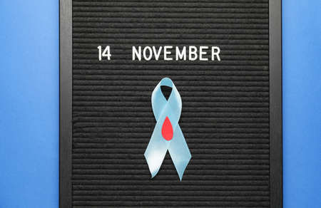Board with awareness ribbon and date of World Diabetes Day on color backgroundの写真素材