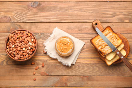 Bowl with tasty peanut butter, toasts and nuts on wooden background