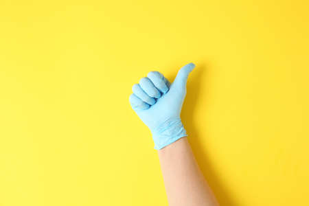 Hand in protective glove showing thumb-up on color background