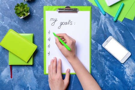 Female hands, clipboard with text MY GOALS and mobile phone on color background