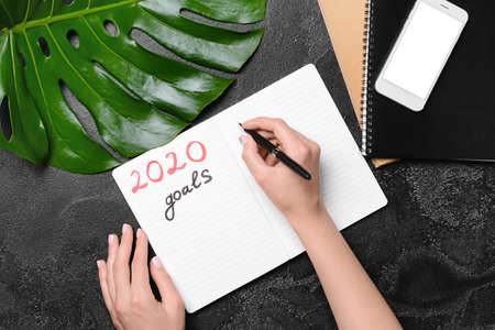 Female hands, text 2020 GOALS in notebook and mobile phone on dark background