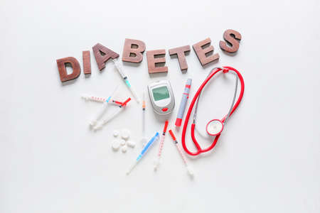 Glucometer with lancet pen, stethoscope, pills, syringes and word DIABETES on white backgroundの写真素材