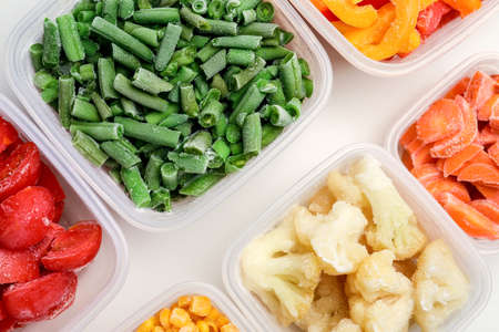 Plastic containers with different frozen vegetables on white background