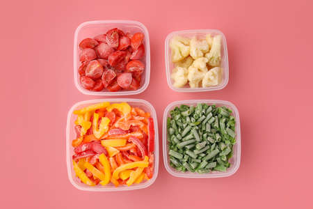Plastic containers with frozen vegetables on color background