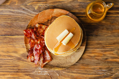 Plate with tasty pancakes and fried bacon on wooden background